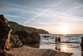A couple stand at the shoreline as they admire the sunset over Plu00e9mont Bay